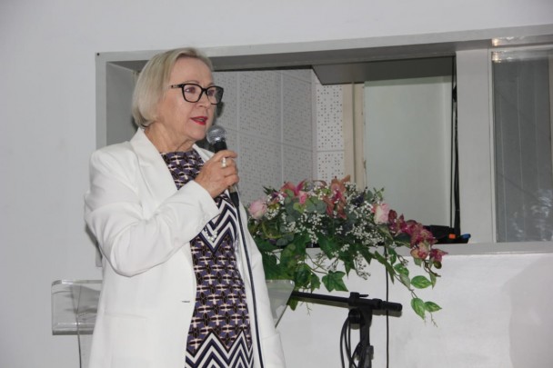 De pé, Secretária Arita fala, segurando o microfone. 